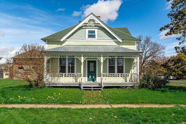 victorian home featuring metal roof, a front lawn, covered porch, and a chimney