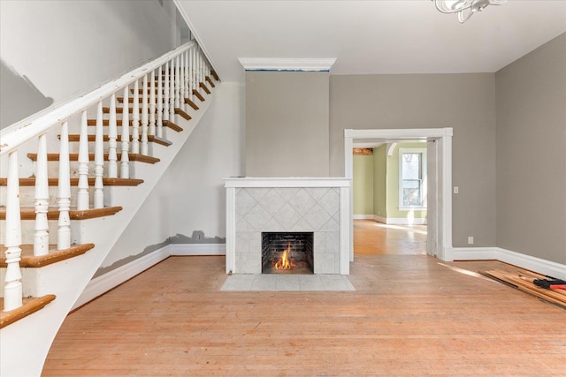 unfurnished living room featuring baseboards, stairway, a tile fireplace, and wood finished floors