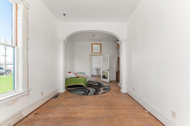 corridor featuring visible vents, baseboards, arched walkways, ornate columns, and wood finished floors