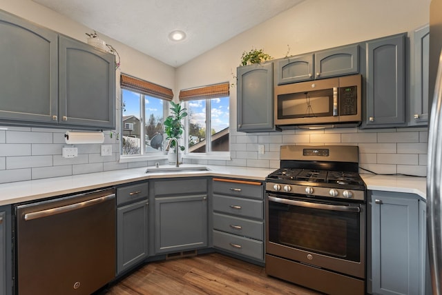kitchen with dark wood finished floors, a sink, lofted ceiling, stainless steel appliances, and gray cabinetry