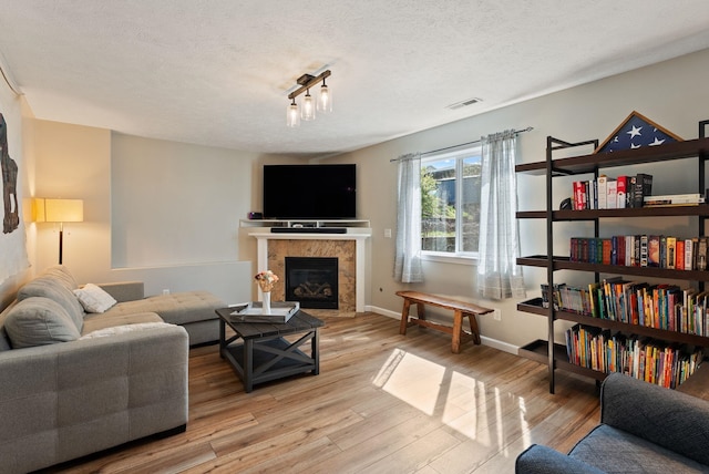 living area featuring baseboards, a fireplace, light wood-style flooring, a textured ceiling, and visible vents