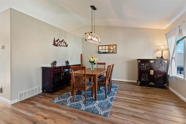 dining space with a notable chandelier, lofted ceiling, visible vents, and wood finished floors
