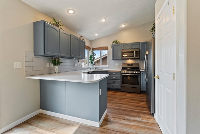 kitchen with light countertops, appliances with stainless steel finishes, a peninsula, gray cabinets, and decorative backsplash