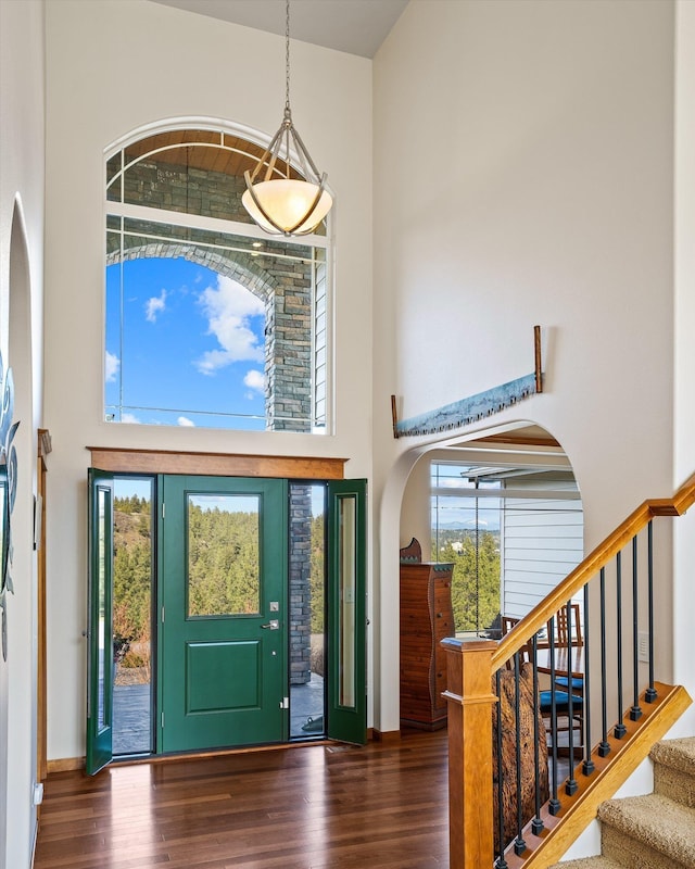 entrance foyer with baseboards, stairway, a high ceiling, arched walkways, and wood finished floors