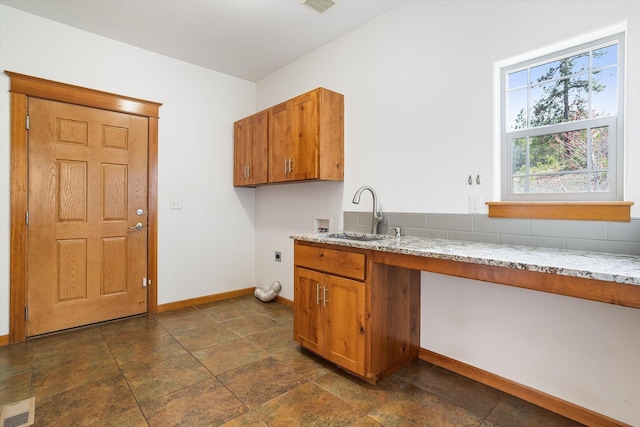 kitchen featuring light stone countertops, brown cabinetry, visible vents, a sink, and baseboards