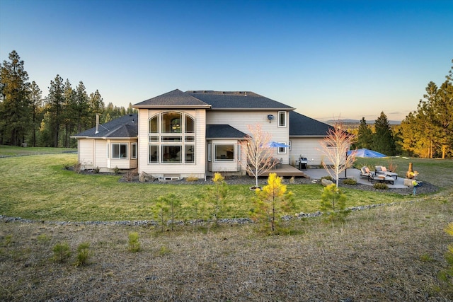 back of property with a shingled roof, a patio, and a lawn
