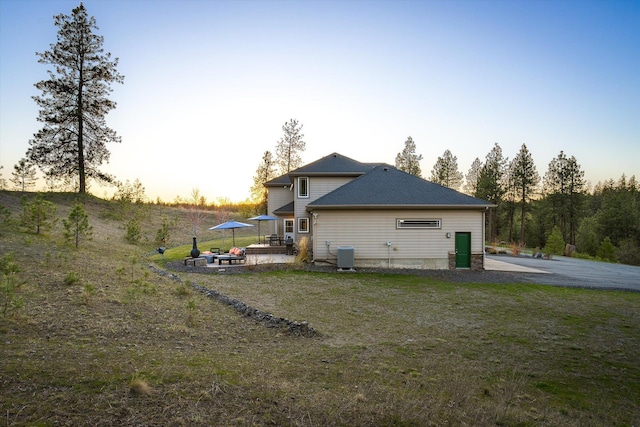 back of house at dusk with central air condition unit, a patio, and a lawn
