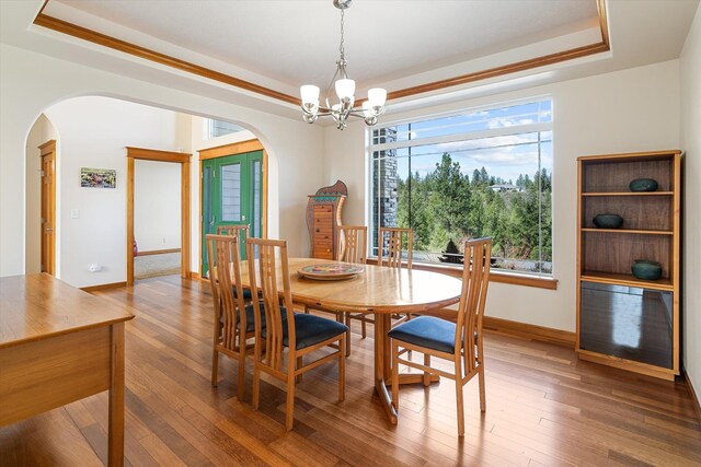 dining room with a notable chandelier, baseboards, a raised ceiling, arched walkways, and wood-type flooring