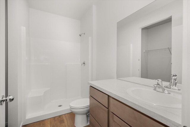 bathroom with toilet, a stall shower, wood finished floors, and vanity