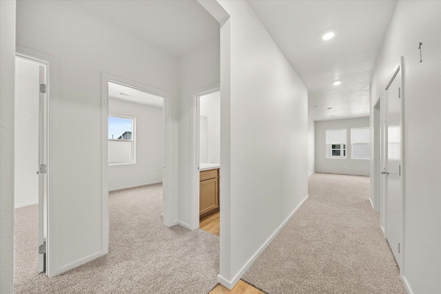 corridor featuring light colored carpet, baseboards, recessed lighting, and a wealth of natural light