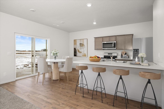 kitchen featuring a kitchen breakfast bar, a peninsula, light wood-style floors, stainless steel appliances, and a sink