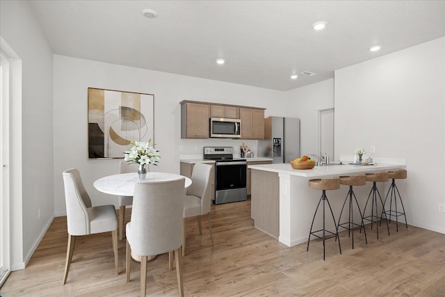 kitchen with light wood-style floors, a peninsula, appliances with stainless steel finishes, and a breakfast bar area