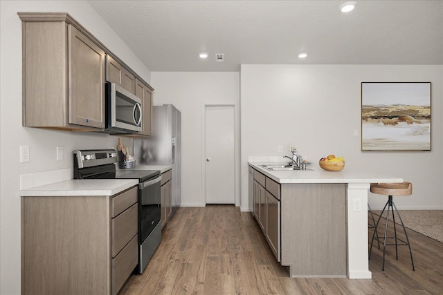 kitchen featuring light wood-style flooring, a breakfast bar, appliances with stainless steel finishes, light countertops, and a sink