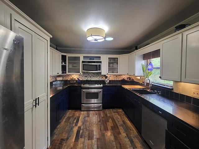 kitchen featuring stainless steel appliances, a sink, dark wood finished floors, dark countertops, and glass insert cabinets