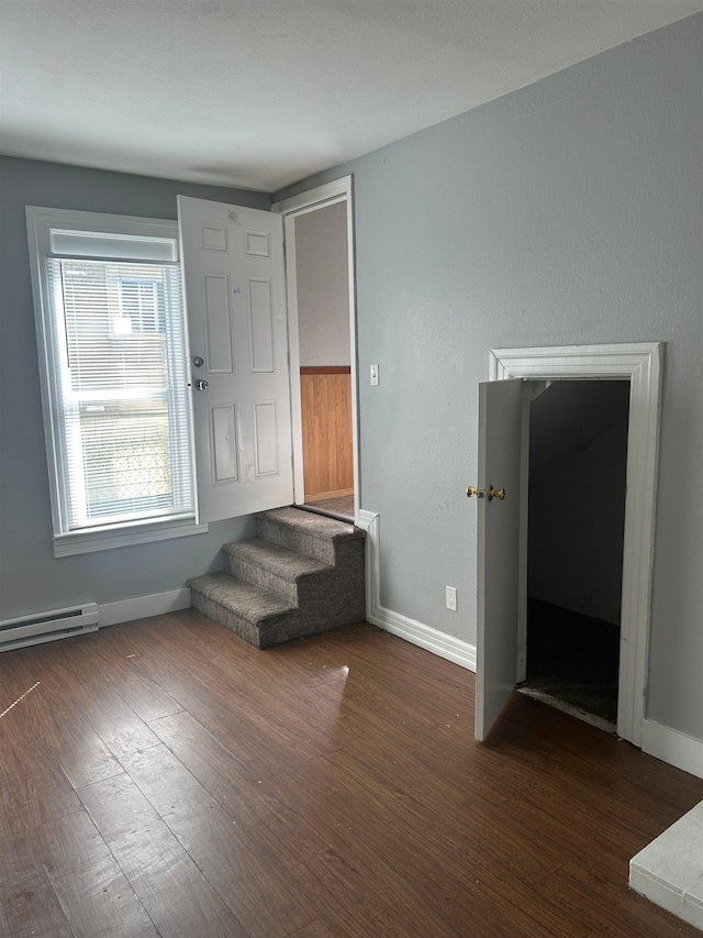 unfurnished room featuring a baseboard radiator, wood finished floors, baseboards, and stairs