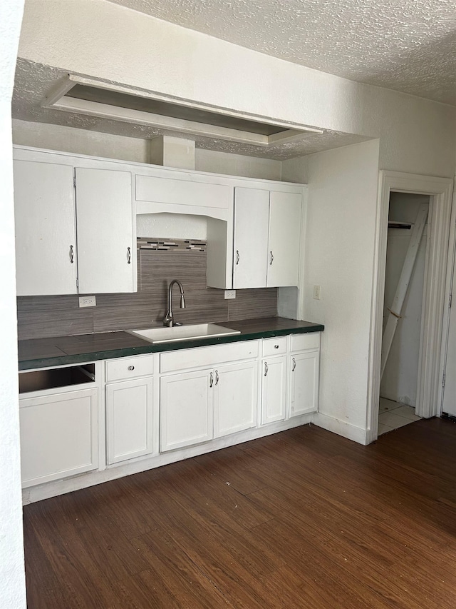 kitchen with white cabinets, a sink, dark wood-style flooring, dark countertops, and a textured ceiling