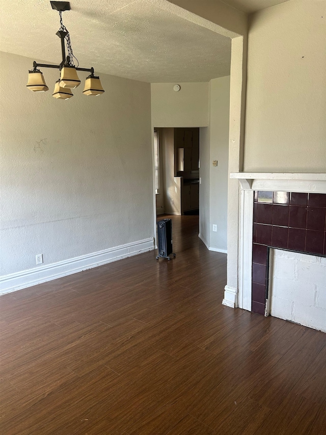 unfurnished living room featuring dark wood-style flooring, baseboards, a tile fireplace, and a textured ceiling