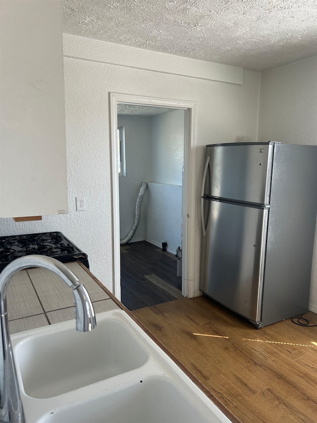 kitchen with freestanding refrigerator, a textured ceiling, wood finished floors, a sink, and a textured wall