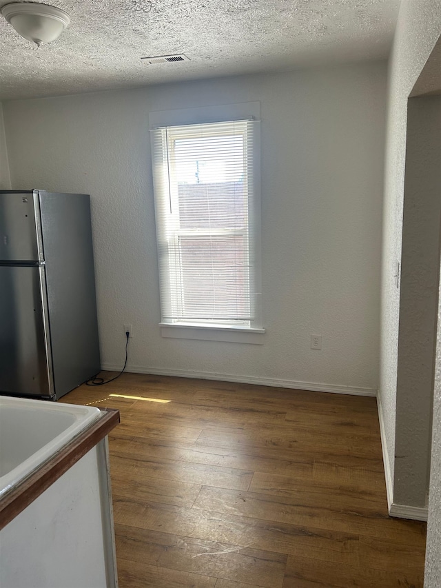 unfurnished dining area with visible vents, baseboards, a textured ceiling, and wood finished floors