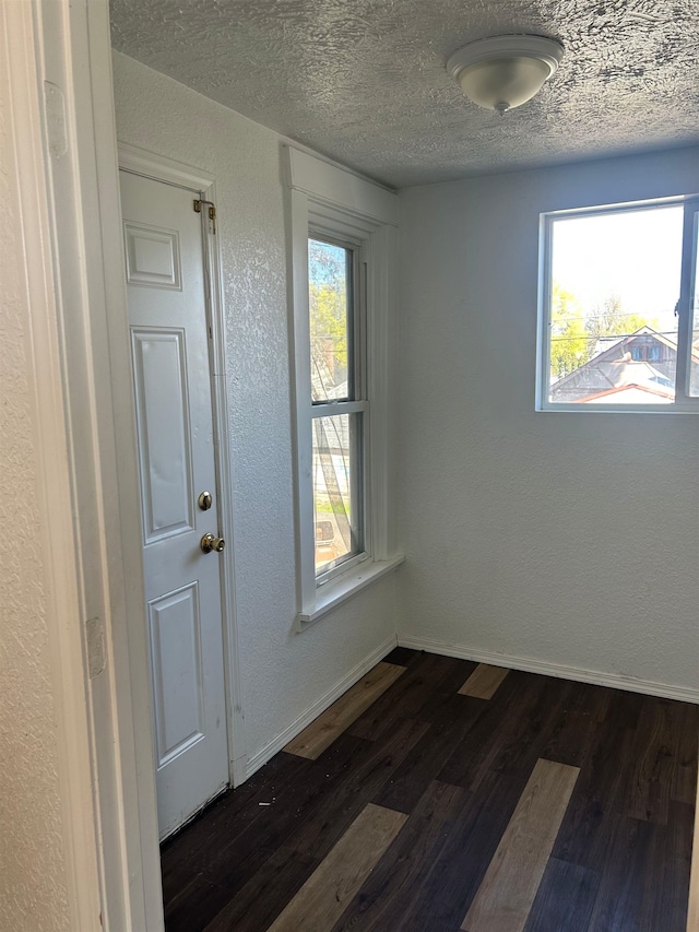unfurnished room with a healthy amount of sunlight, dark wood-style floors, a textured wall, and a textured ceiling
