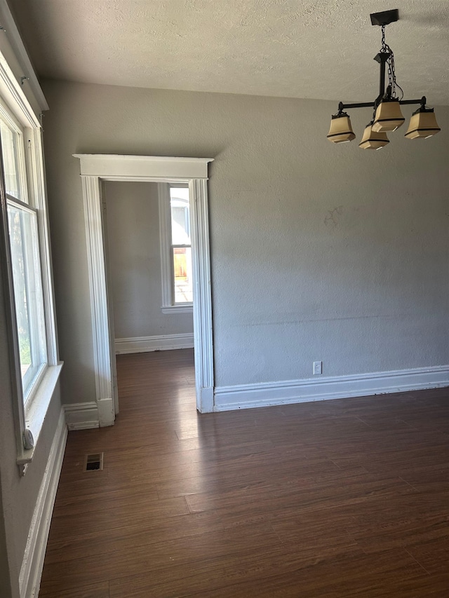 empty room with visible vents, baseboards, a notable chandelier, a textured ceiling, and dark wood finished floors