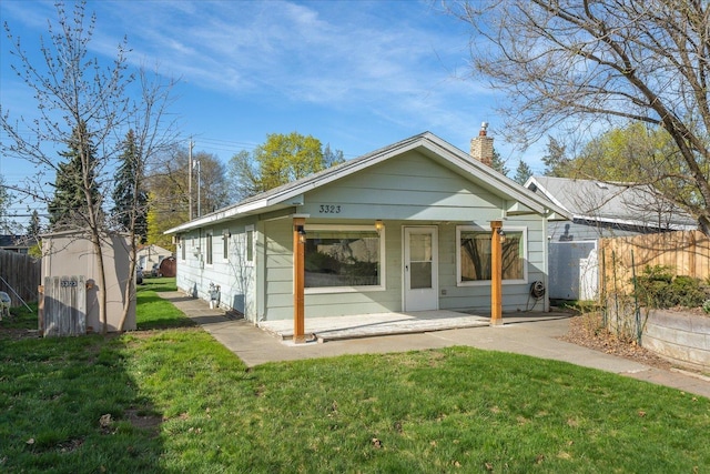back of house with an outbuilding, a chimney, fence, and a lawn