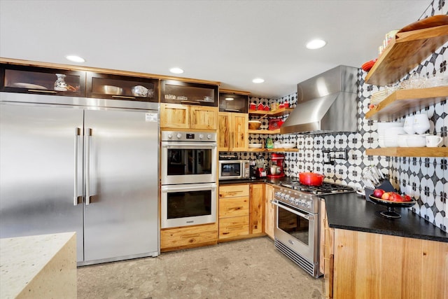 kitchen featuring wall chimney exhaust hood, open shelves, dark countertops, premium appliances, and decorative backsplash