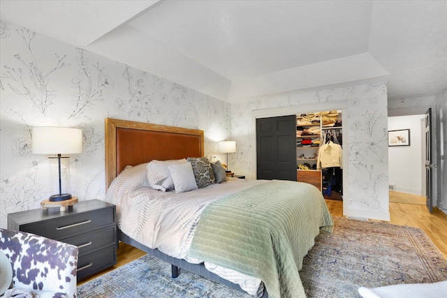 bedroom featuring wallpapered walls, wood finished floors, a closet, and a spacious closet