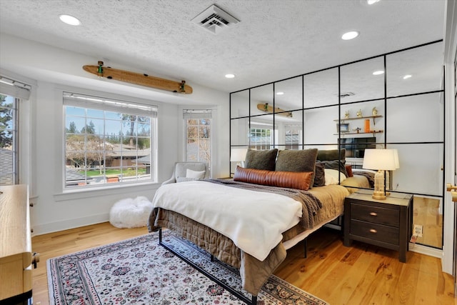 bedroom featuring light wood-style floors, multiple windows, visible vents, and a textured ceiling