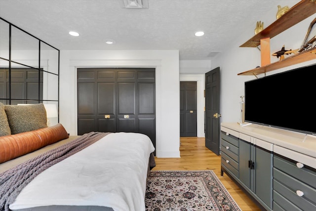 bedroom featuring a closet, recessed lighting, light wood-type flooring, and a textured ceiling