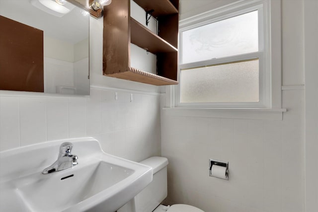 bathroom with tile walls, a sink, and toilet