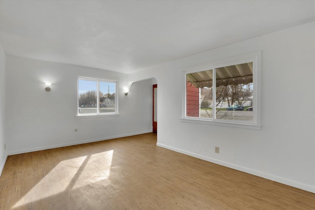 spare room featuring baseboards, arched walkways, and wood finished floors