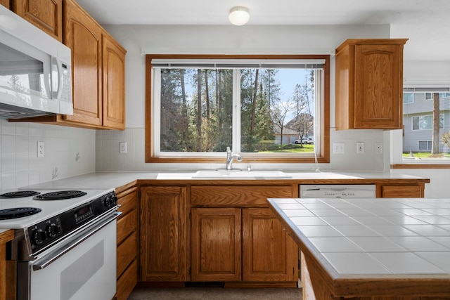 kitchen featuring a sink, tile countertops, tasteful backsplash, and white appliances