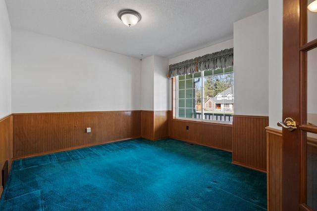 carpeted empty room featuring a textured ceiling, wood walls, and a wainscoted wall