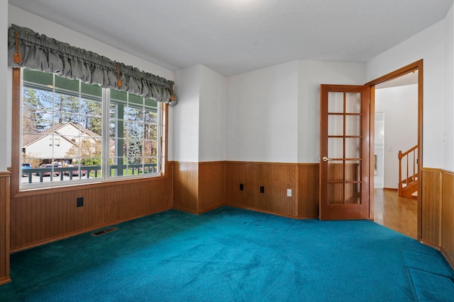 unfurnished room with wooden walls, visible vents, carpet flooring, and wainscoting