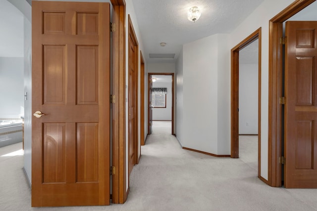 hall featuring a textured ceiling, light colored carpet, and baseboards