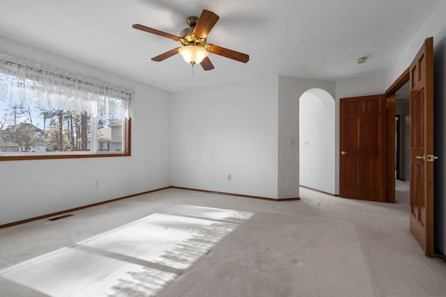 spare room featuring visible vents, a ceiling fan, arched walkways, and light colored carpet