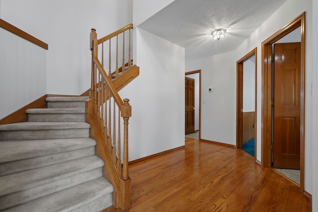 stairs featuring a textured ceiling, wood finished floors, and baseboards