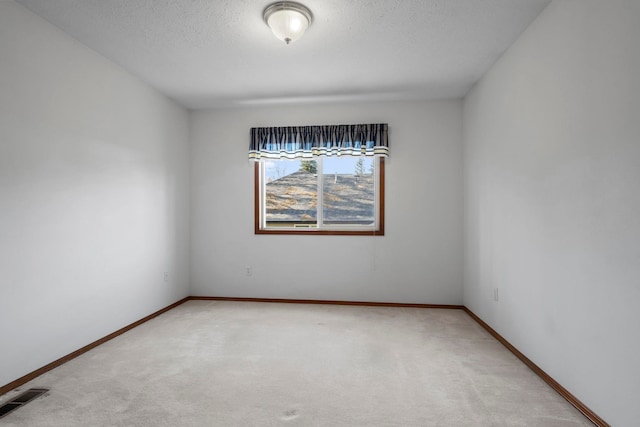 spare room with baseboards, visible vents, light colored carpet, and a textured ceiling