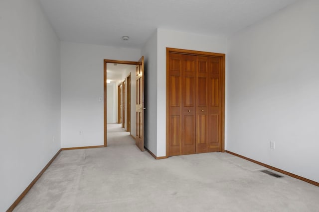 unfurnished bedroom with a closet, baseboards, light colored carpet, and visible vents