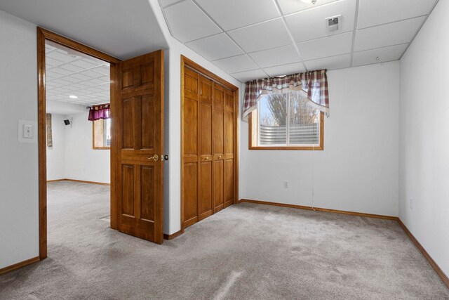 unfurnished bedroom featuring a closet, light colored carpet, baseboards, and a drop ceiling