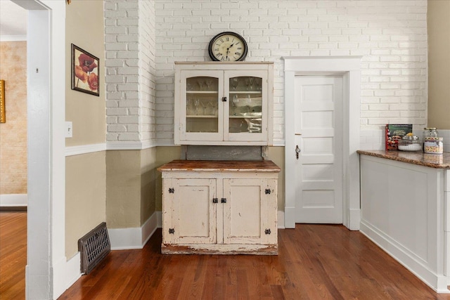 bar featuring visible vents, baseboards, dark wood-style floors, and brick wall