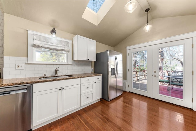 kitchen featuring white cabinets, dark wood finished floors, a sink, lofted ceiling with skylight, and appliances with stainless steel finishes