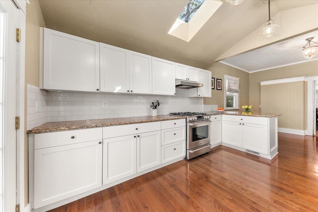kitchen with white cabinets, a peninsula, lofted ceiling with skylight, stainless steel gas stove, and under cabinet range hood