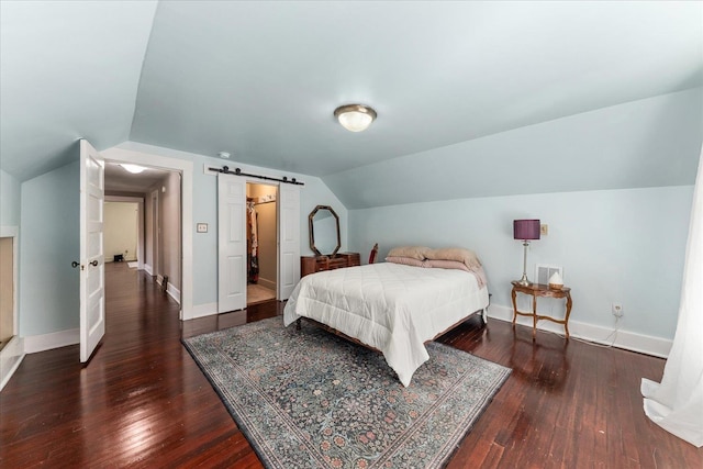 bedroom with a barn door, vaulted ceiling, hardwood / wood-style floors, and baseboards