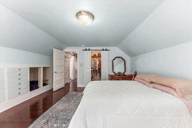 bedroom with lofted ceiling, dark wood-style floors, a walk in closet, and a barn door