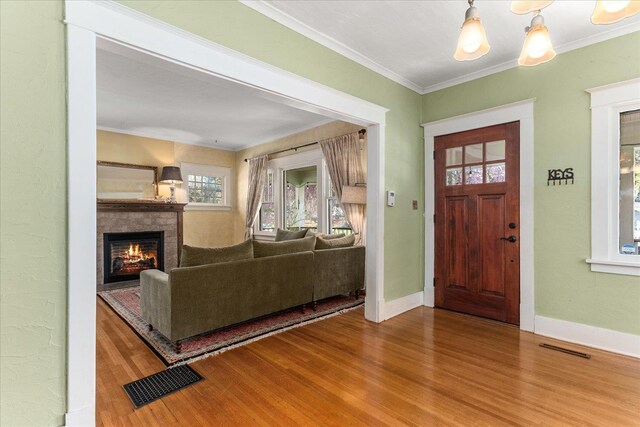 foyer with crown molding, a lit fireplace, wood finished floors, and visible vents
