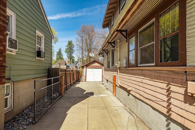 view of side of home featuring fence, driveway, an outdoor structure, and a detached garage
