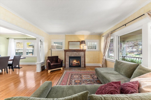 living area with a tile fireplace, baseboards, ornamental molding, and wood finished floors