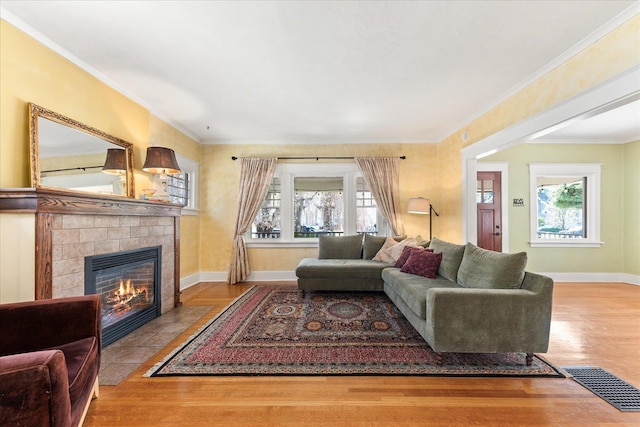 living room featuring wood finished floors, visible vents, crown molding, baseboards, and a tiled fireplace
